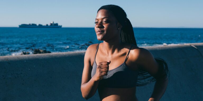 L'image présente une femme qui fait du jogging. Son expression faciale démontre un sentiment de calme, de bien-être. Le fond est la mer, qui présente le calme aussi.
